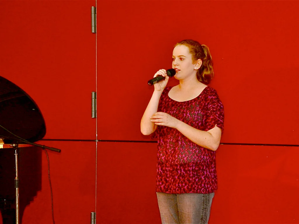 Eine Sängerin singt ins Mikrofon vor der roten Wand.